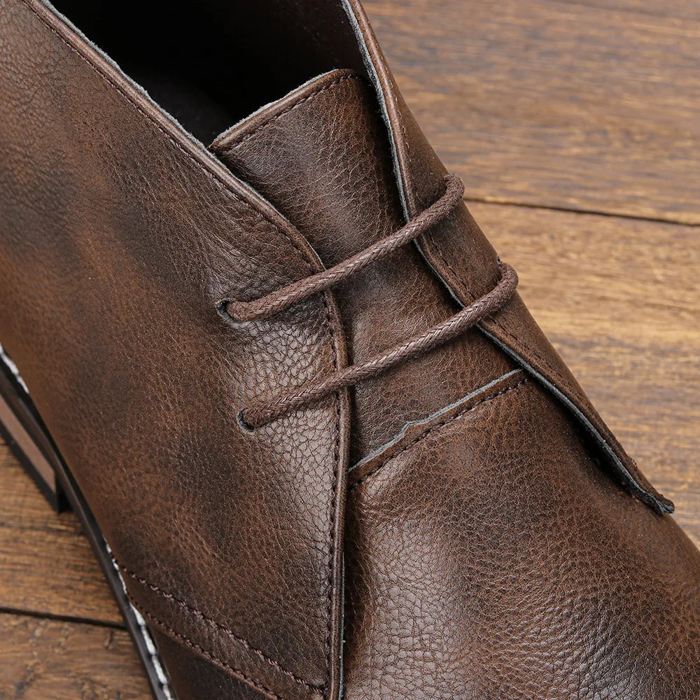 Close-up of the laces and eyelets on a dark brown leather chukka boot, resting on a wooden surface.