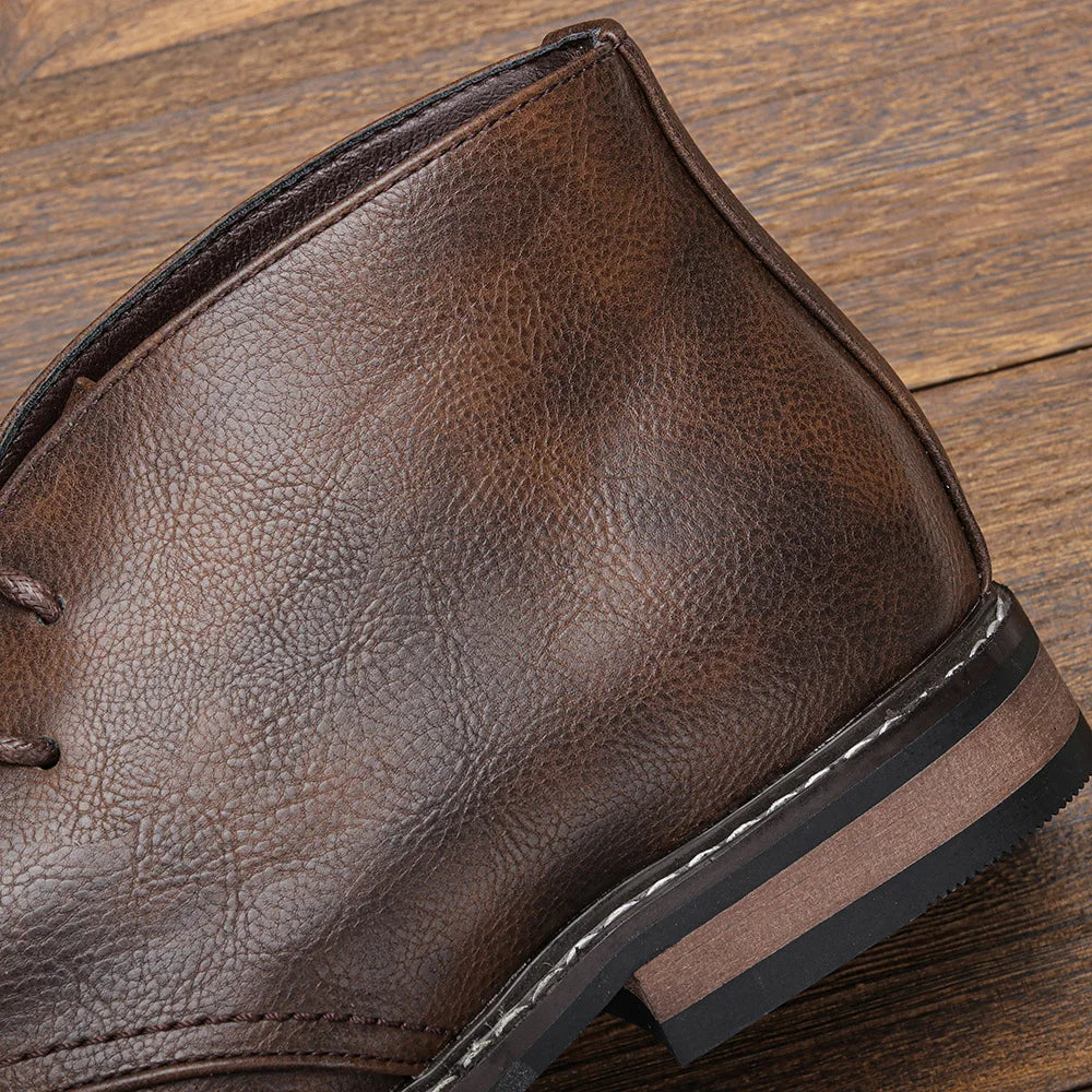 Extreme close-up of the heel and stacked leather sole of a dark brown chukka boot, resting on a wooden surface.