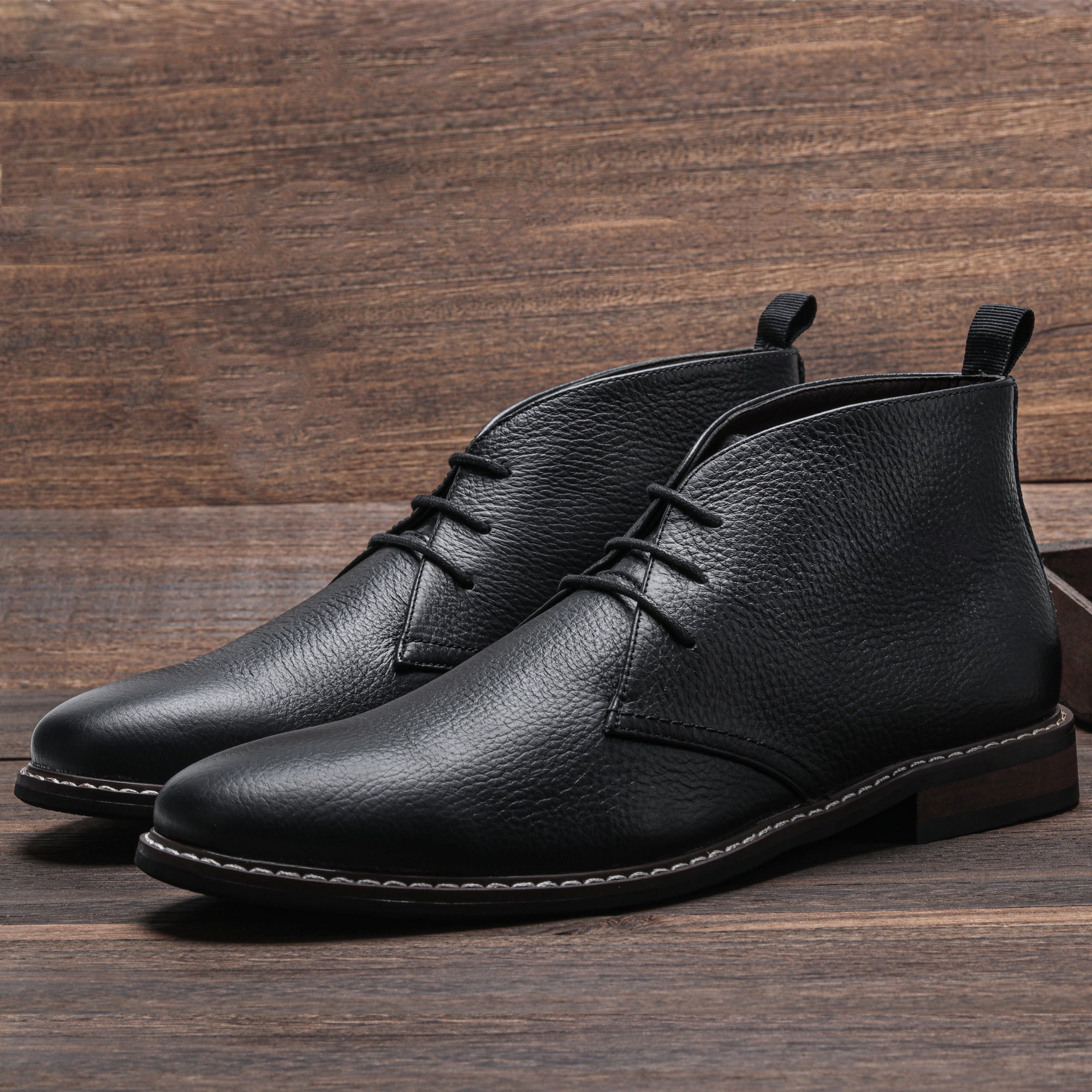 Pair of black pebbled leather lace-up chukka boots on a wooden plank floor.