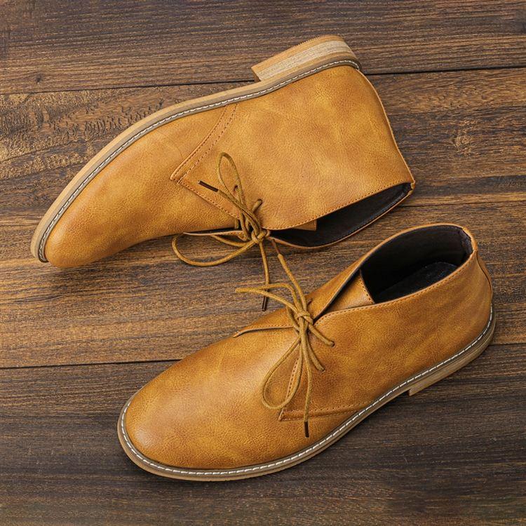 Overhead view of a pair of tan leather lace-up chukka boots lying on a wooden plank surface, laces untied.