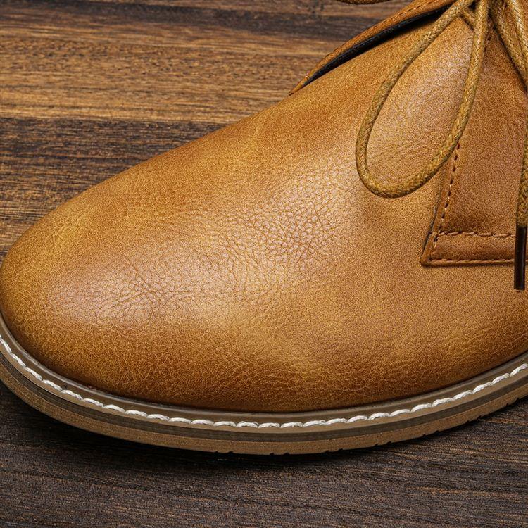 Extreme close-up of a tan leather chukka boot's toe and stitched sole detail, with laces visible in the background.