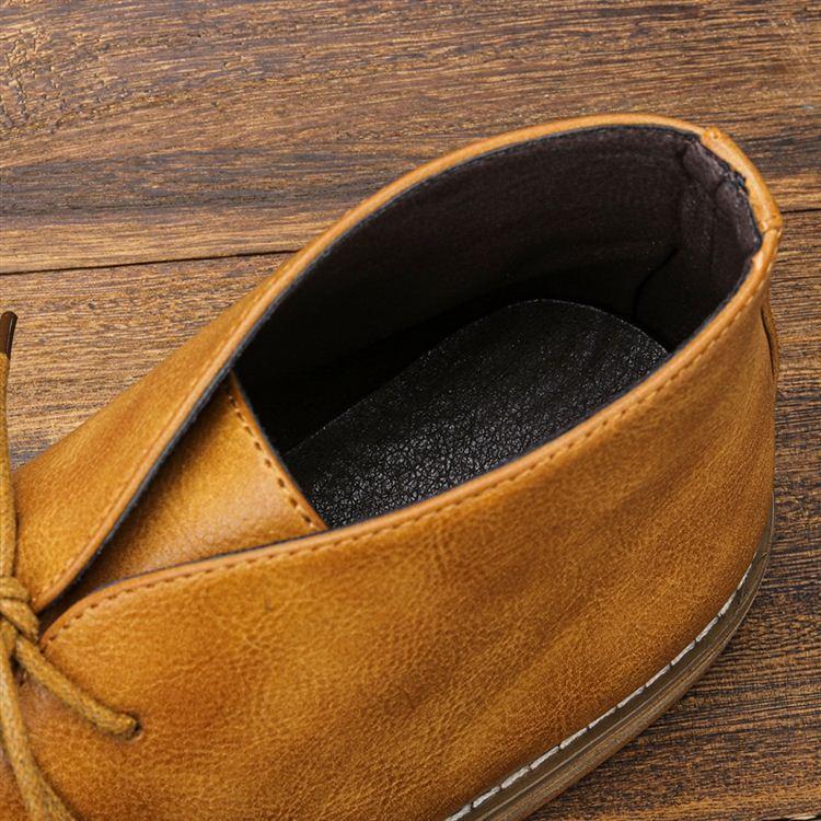 Close-up looking down into the opening of a tan leather chukka boot, showing the black interior lining, on a wooden surface.