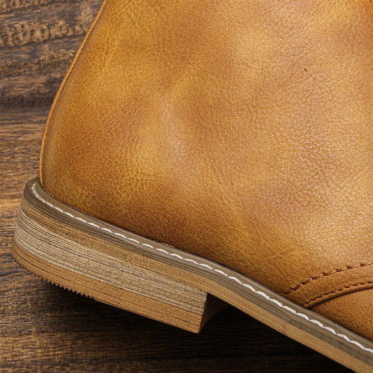 Extreme close-up of the heel and stacked leather sole of a tan chukka boot, resting on a wooden surface.