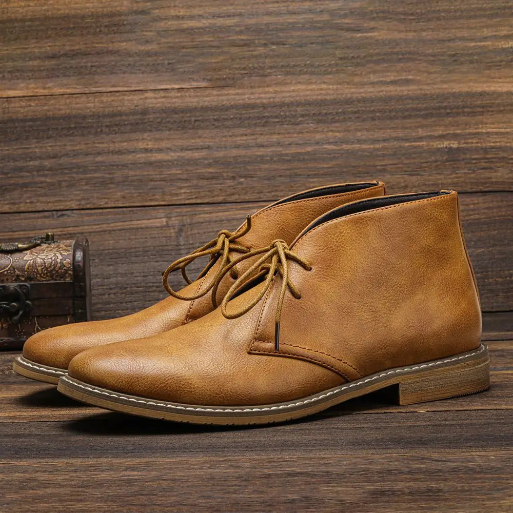 Pair of tan leather lace-up chukka boots resting on a wooden surface beside a small carved wooden chest.