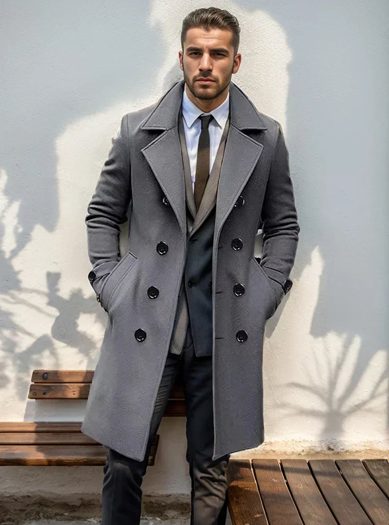 Gray wool double-breasted trench coat with structured lapels and a tailored mid-length fit worn over a suit.