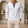 Man wearing a white long-sleeve Henley sweater with a contrast navy placket and collar trim, three-button neckline, and modern slim fit.