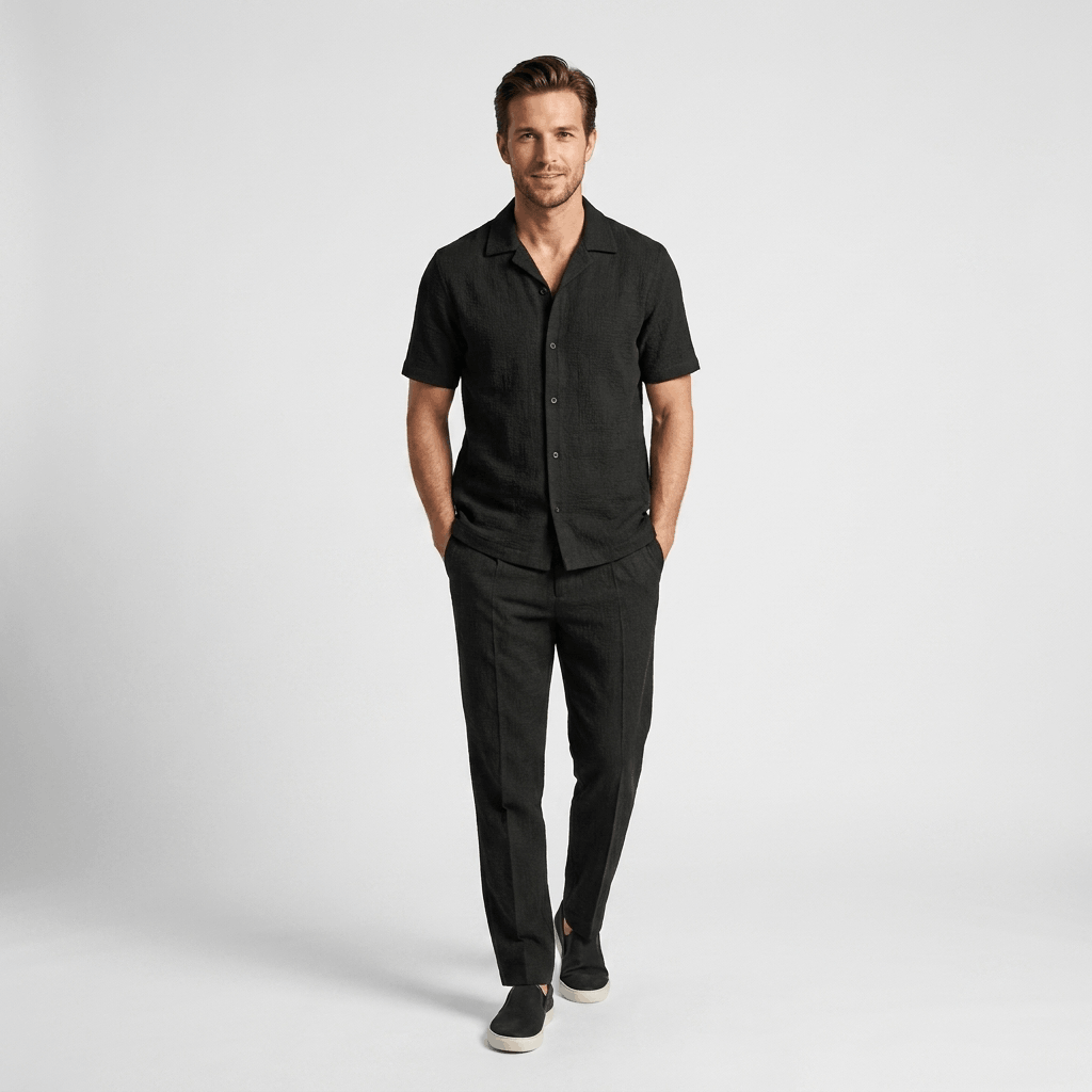 Man wearing a black short-sleeve cotton shirt with matching black trousers and white sneakers.