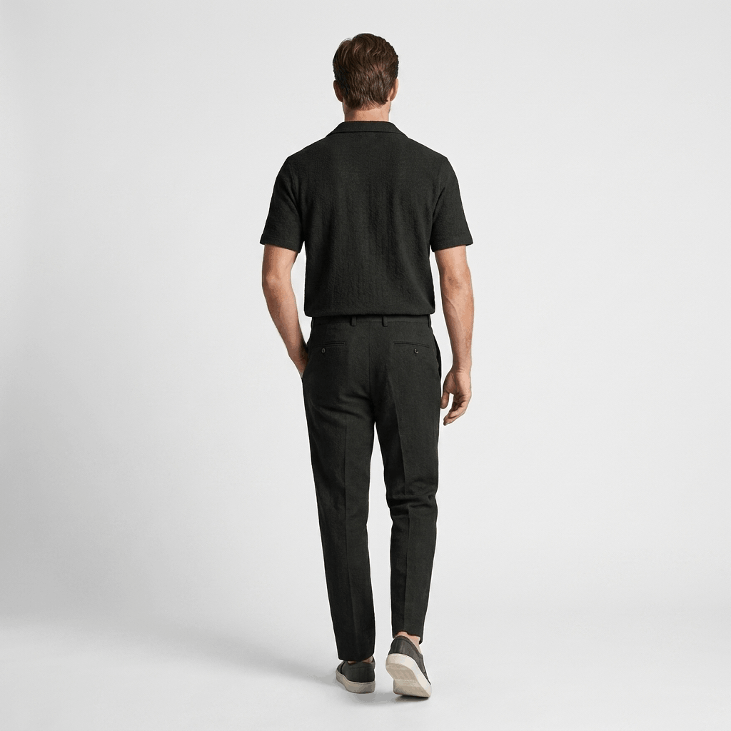 Back view of a man wearing a black cotton short-sleeve shirt with matching black trousers.