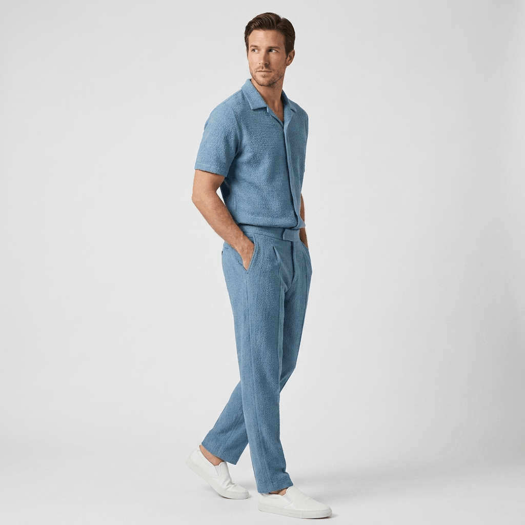 Man wearing a light blue short-sleeve cotton shirt with matching linen trousers in a relaxed side pose.