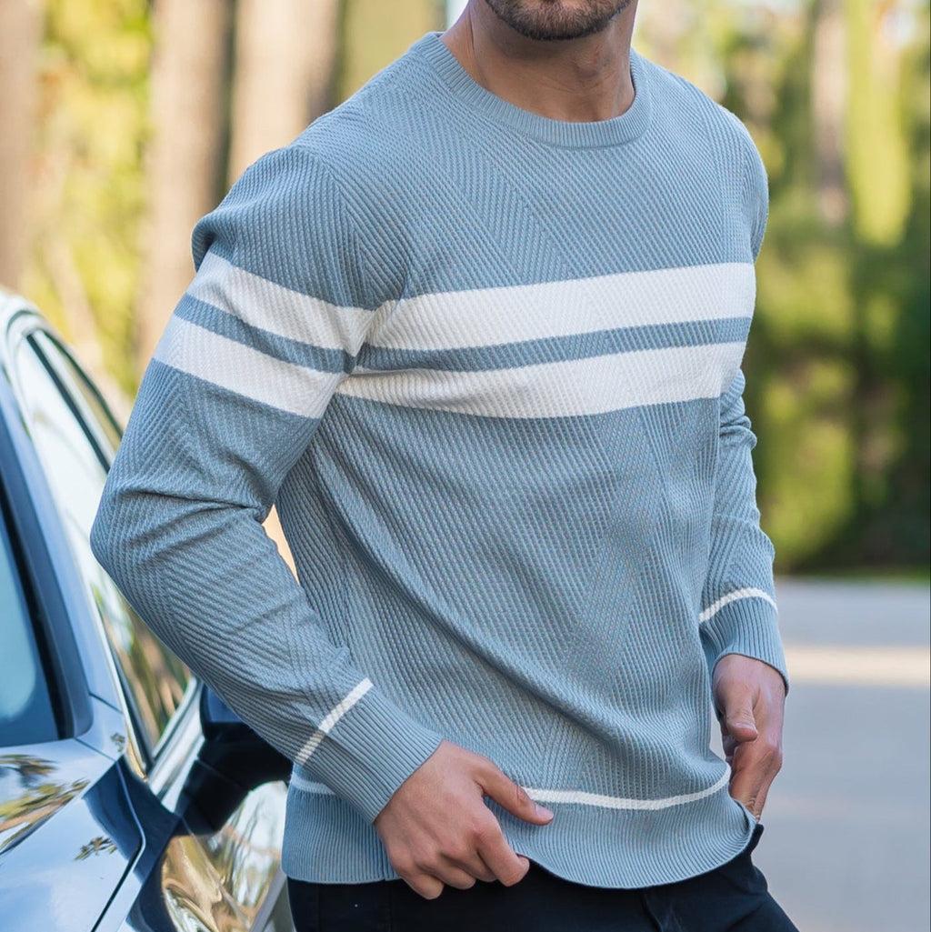Man wearing light blue striped crewneck knit sweater outdoors, close-up torso view with backpack strap