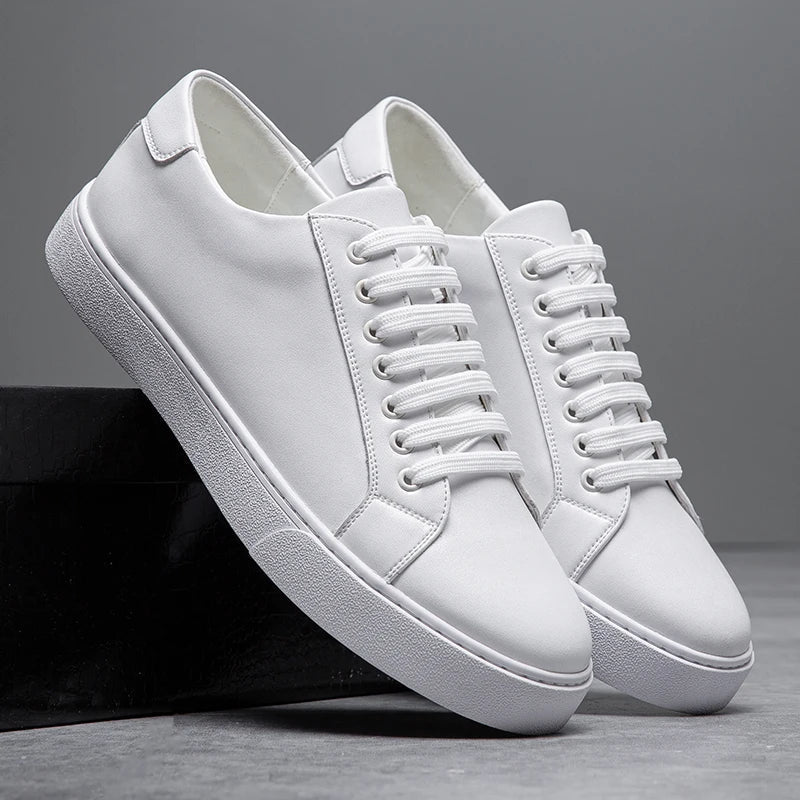 Pair of white leather Zoren sneakers with matching white soles, one shoe leaning against a black box in studio setting