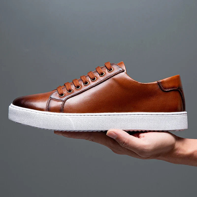 Hand holding a single brown leather Zoren sneaker, showing side profile with tonal stitching and white sole