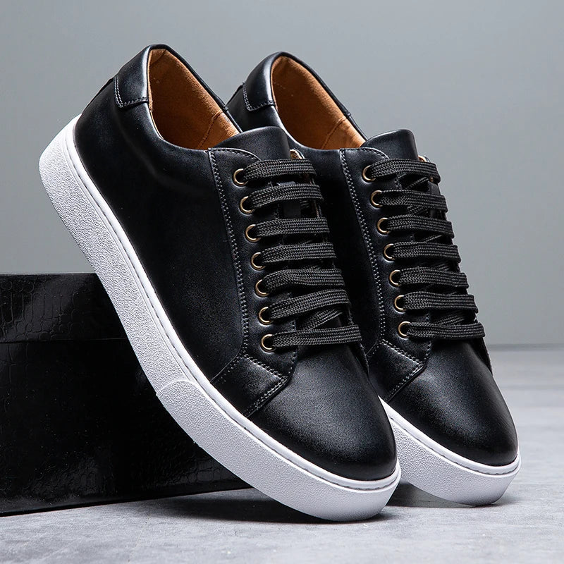 Pair of black leather Zoren sneakers with white soles, one shoe leaning against a black box in studio setting