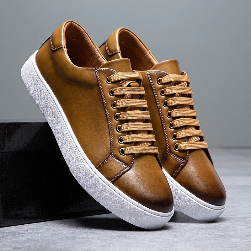 Pair of tan leather Zoren sneakers with white soles, one shoe leaning against a black box in studio setting
