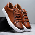 Pair of brown leather Zoren sneakers with white soles, one shoe leaning against a black box in studio setting